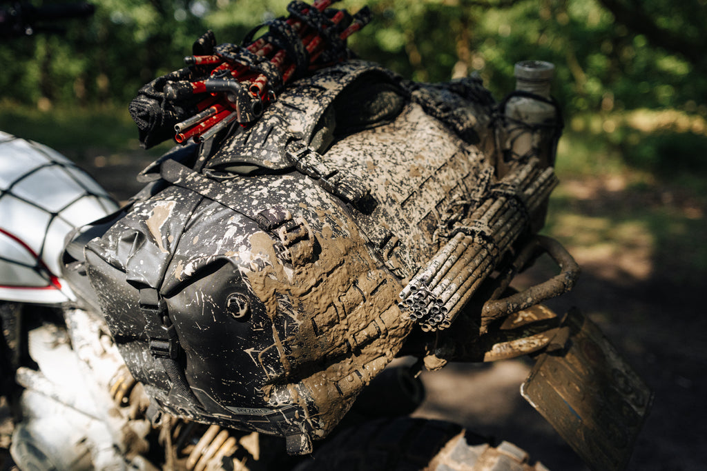 Mud-covered RYZVOX FAR Duffel Bag 40L Moto strapped to a motorcycle rear rack after an off-road ride