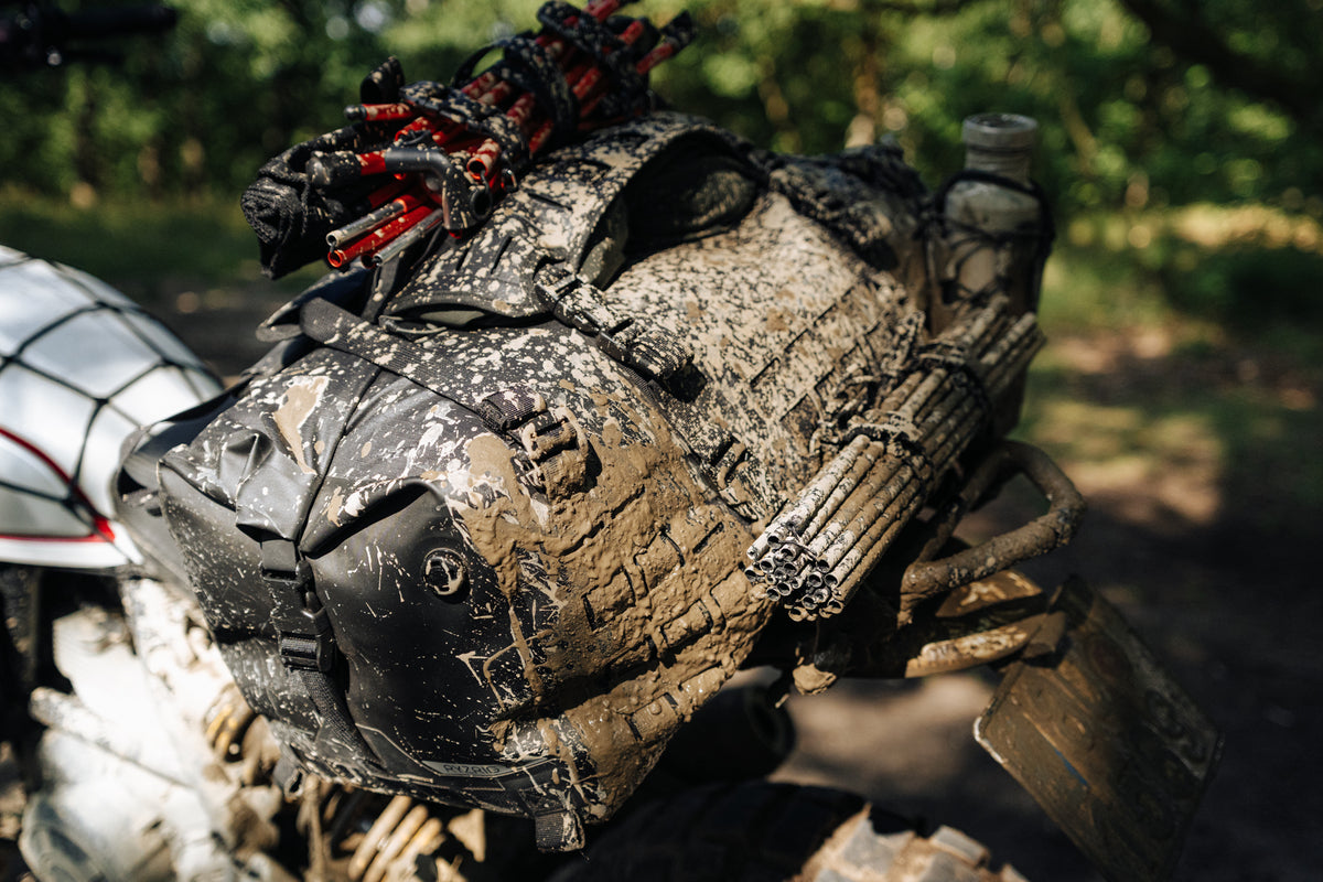 Mud-covered RYZVOX FAR Duffel Bag 40L Moto strapped to a motorcycle rear rack after an off-road ride