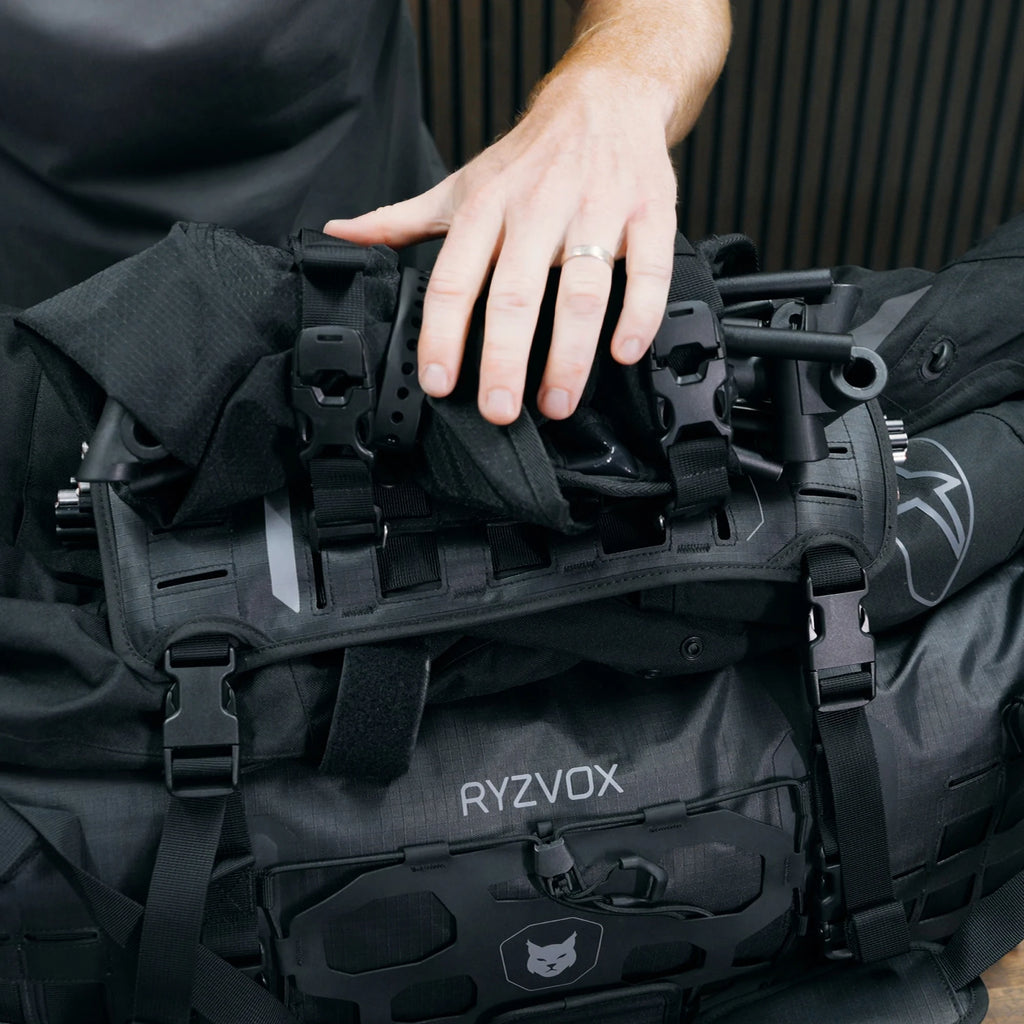 Hand pressing a jacket and tent poles under the RYZVOX FAR Beaver Tail 40L on the duffel bag