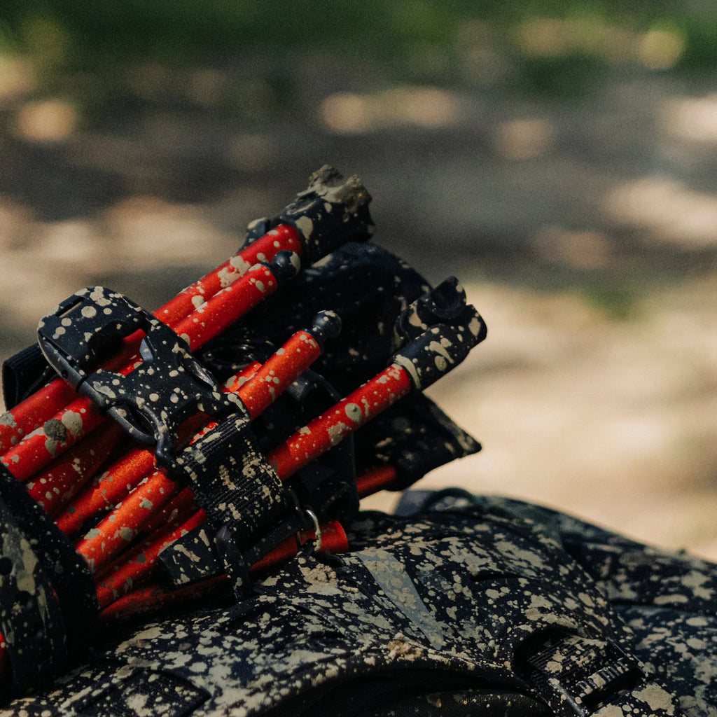 RYZVOX Accessory Straps holding tent poles to a mud-splattered duffel bag on a forest trail