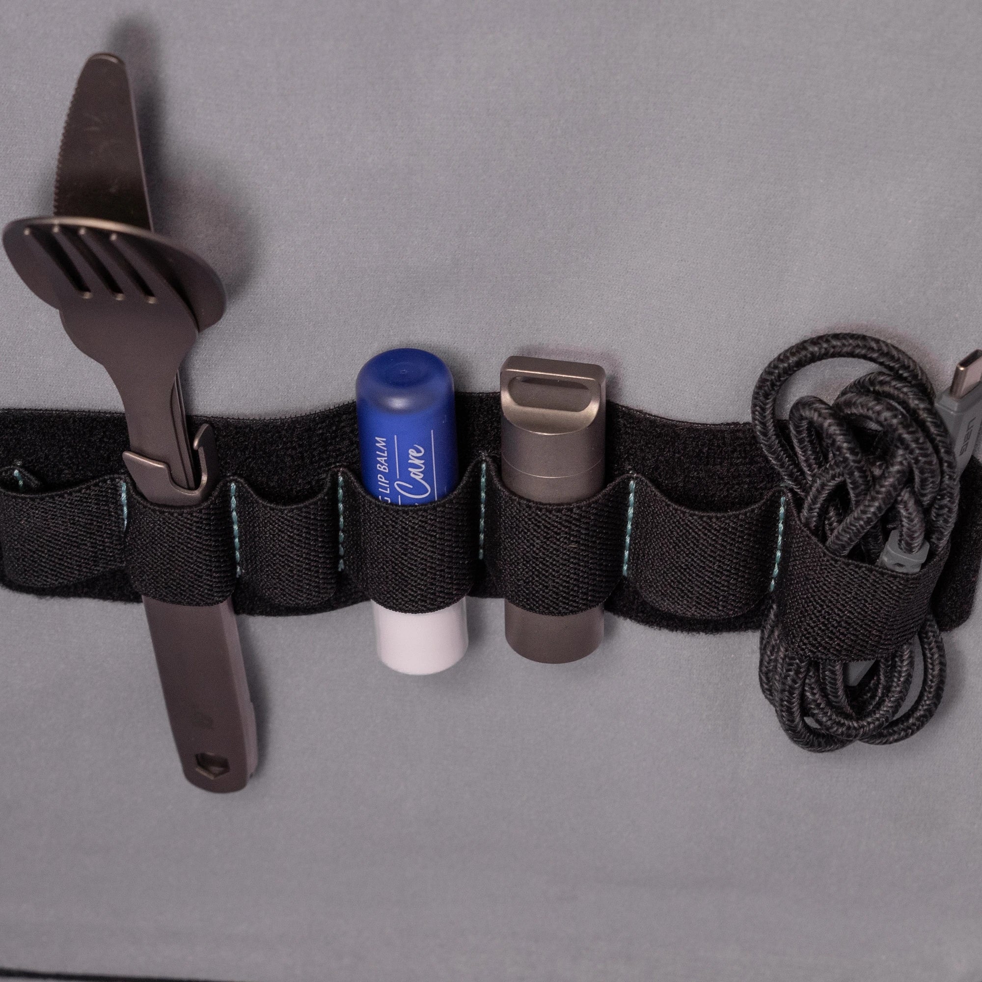 Elastic organizer holding cutlery, a lighter and a coiled cable inside a RYZVOX bag