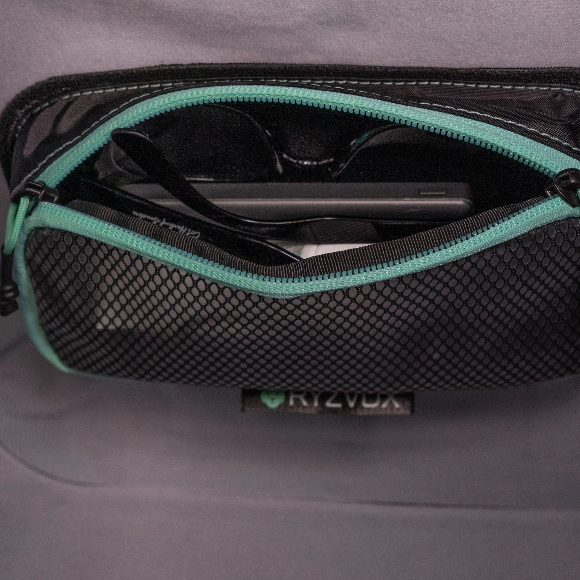 Mesh pouch open inside a RYZVOX bag, holding a phone and sunglasses