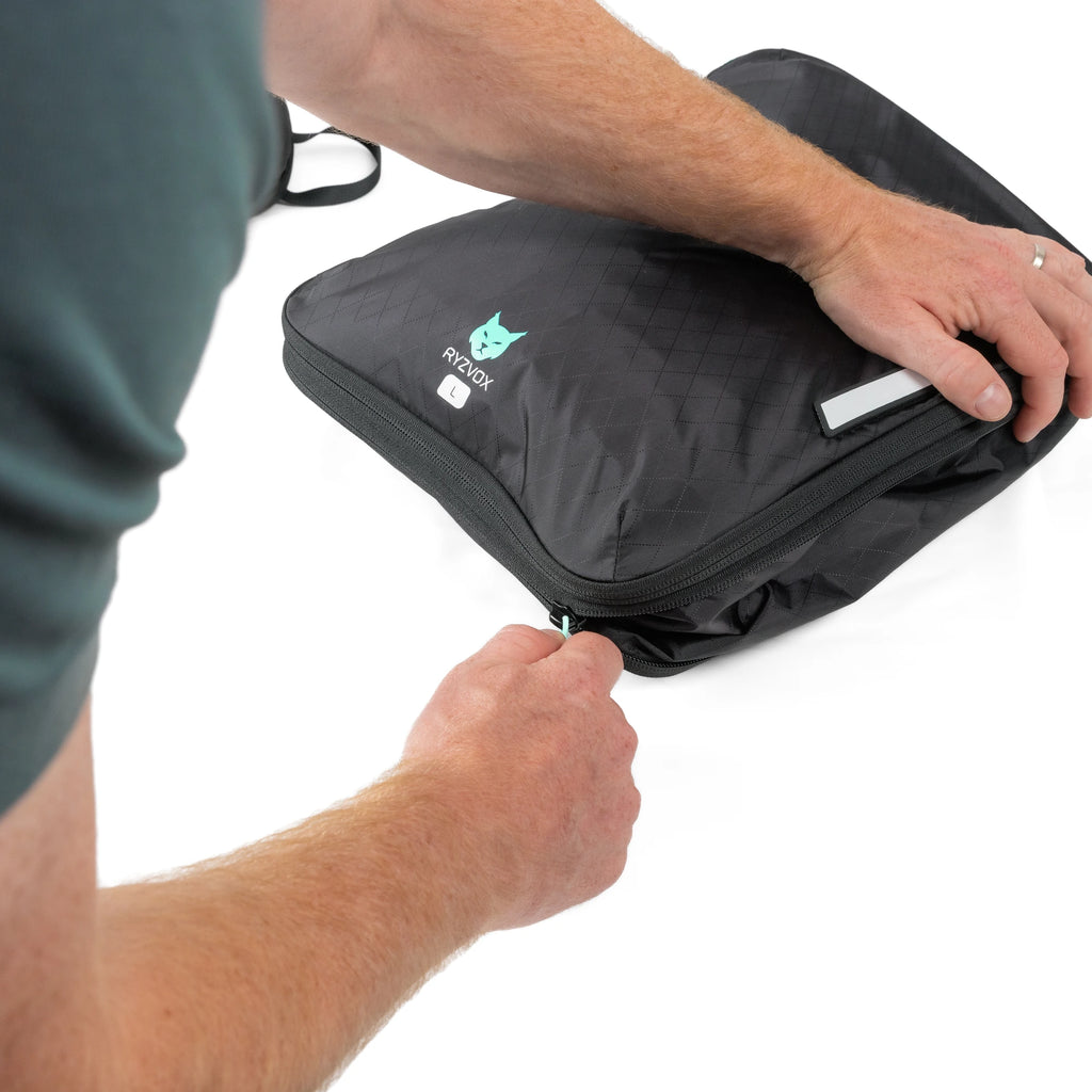 Person pulling the compression zip closed on a packed RYZVOX Packing Cube L