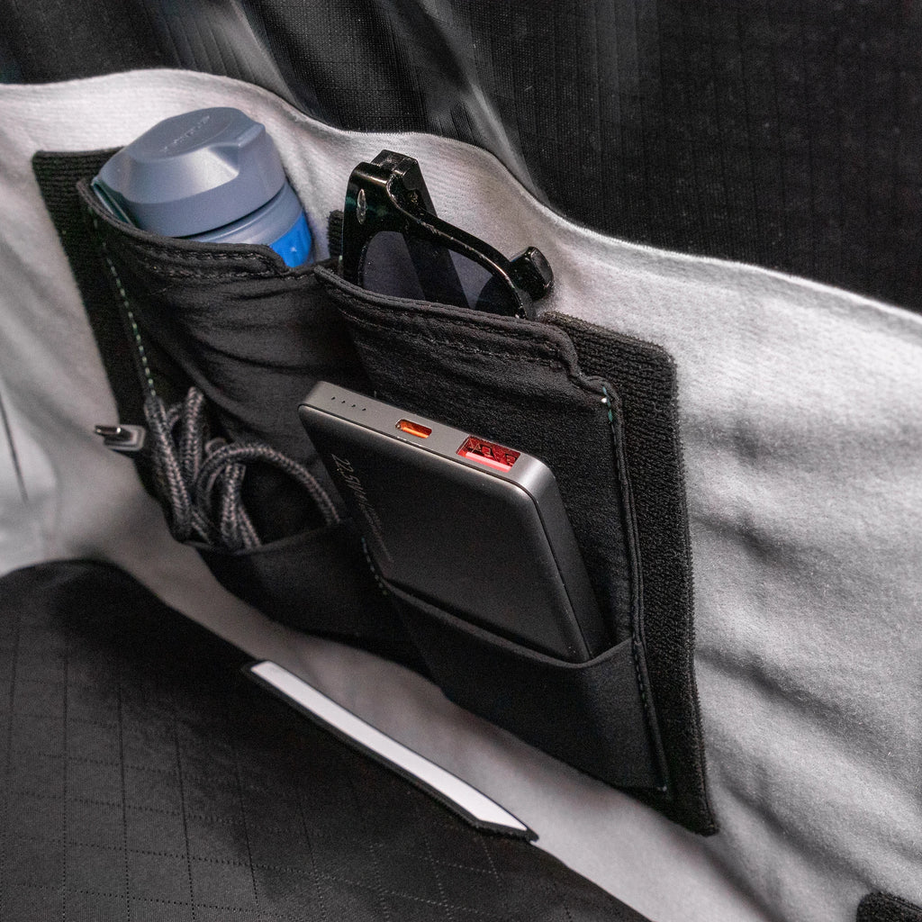 Stretch pocket mounted inside a RYZVOX bag, holding a bottle, sunglasses and a power bank