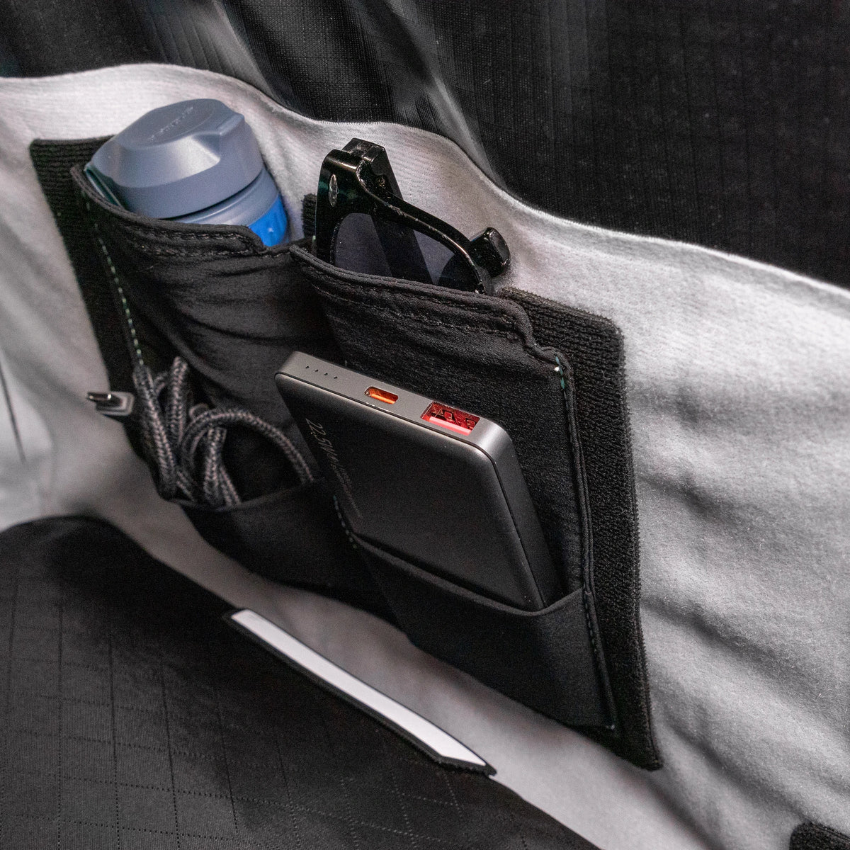 Stretch pocket mounted inside a RYZVOX bag, holding a bottle, sunglasses and a power bank