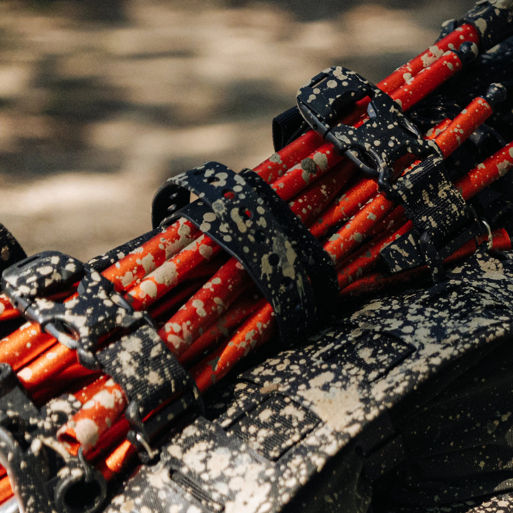 RYZVOX Utility Straps clamped over tent poles on a mud-splattered duffel bag, close view